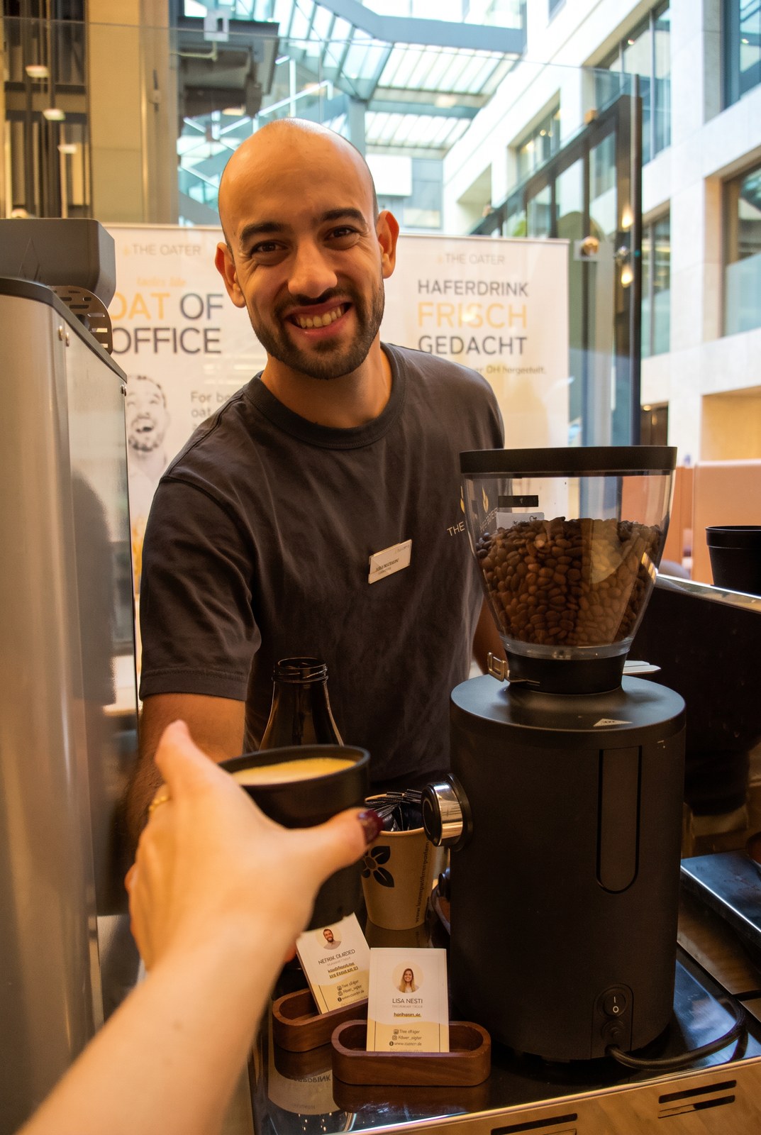 Henrik lächelt in die Kamera und reicht einen Kaffee über die The Oater Kaffeebar