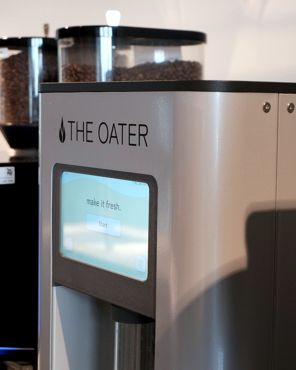 The Oater Maschine mit Touchscreen direkt neben einer professionellen Kaffeemaschine