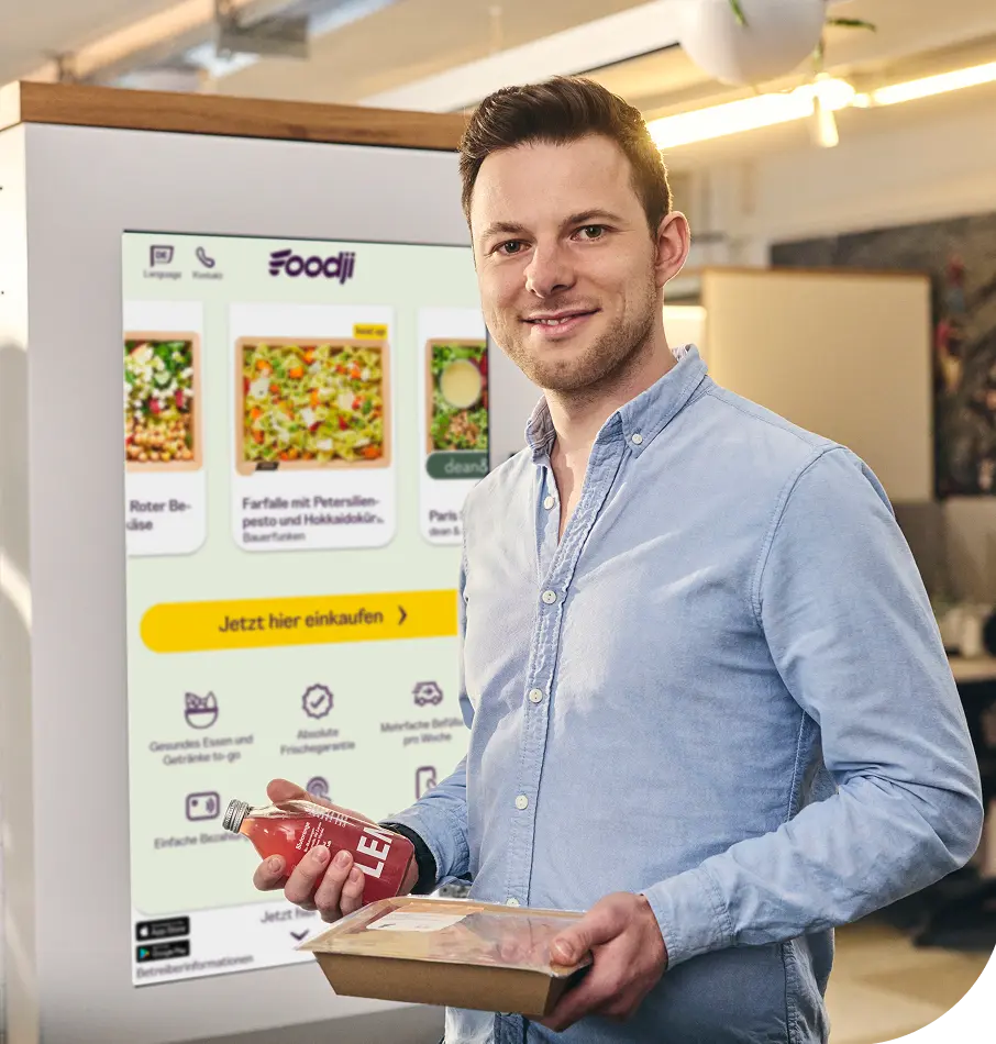 Mann hält eine Mahlzeit vor einem Foodji-Verpflegungsautomaten