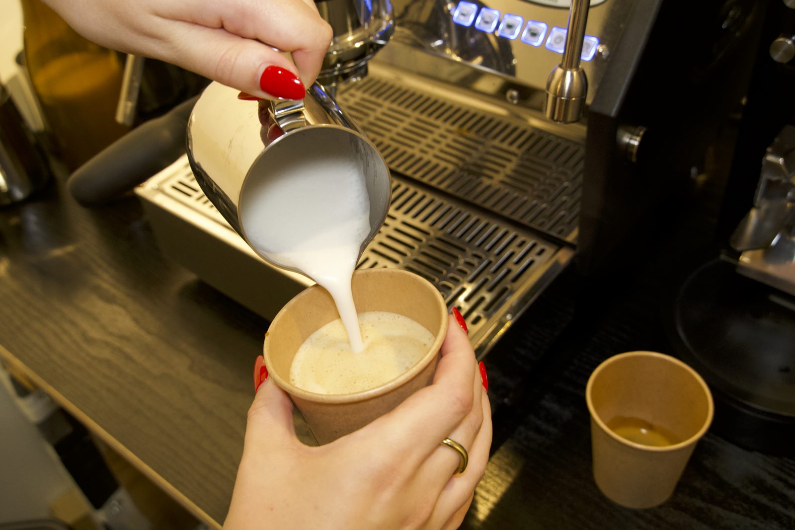 Aufgeschäumter Haferdrink wird aus einem Kännchen in einen Kaffeebecher gegossen