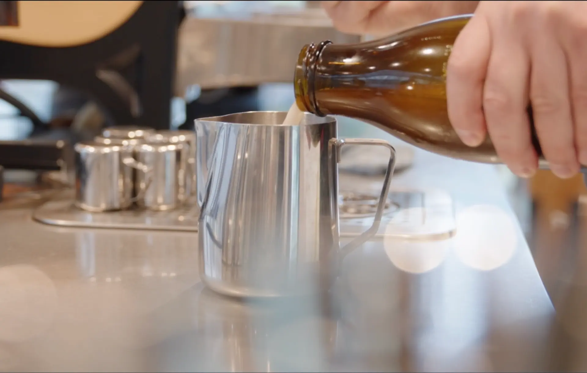 Haferdrink wird aus einer braunen Glasflasche in ein Edelstahlkännchen gegossen