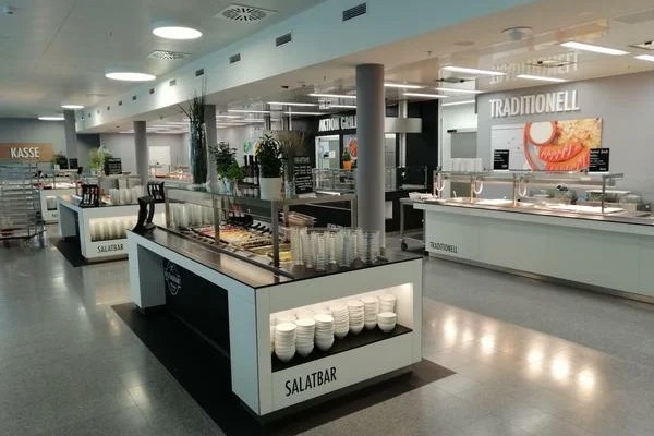 Helle Kantine mit Salatbar und Ausgabetheken unter Deckenleuchten