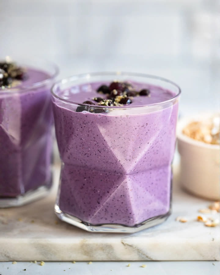 Violetter Blueberry Oat Shake im Glas, garniert mit Blaubeeren und Saaten