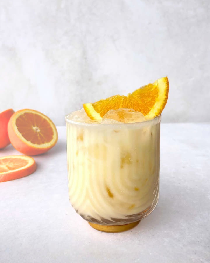 Icy Oat Orange im Glas mit Eis und Orangenspalte, daneben halbierte Orangen